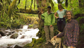 Three women and a dog hiking along a forested stream.